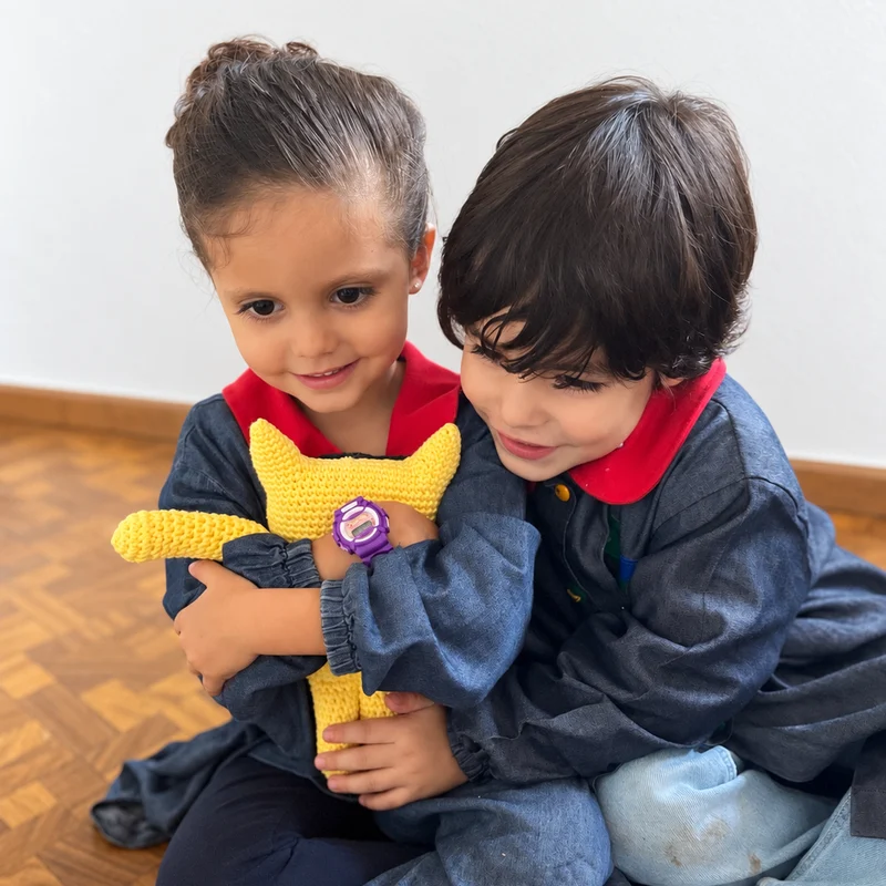 Dos peques de Pirulí abrazados con un gato de peluche amarillo